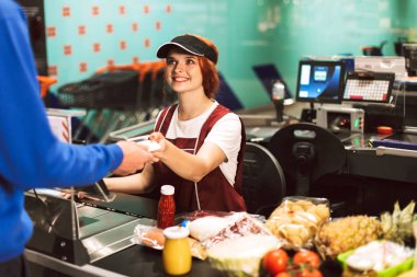 Modern süpermarkette çalışan müşteri mutlu bir şekilde bakarak Üniformalı gülümseyen güzel kadın kasiyer