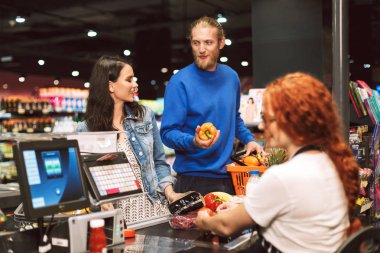 Genç çift ayakta mutlu bir şekilde ürün satın alma birlikte modern markette kasiyer Resepsiyon yakınındaki gülümseyen