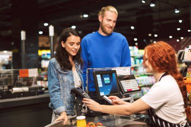 Genç çift ayakta mutlu modern süpermarkette kredi kartıyla ürünler için ödeme kasiyer Resepsiyon yakınındaki gülümseyen