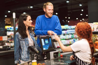Genç çift ayakta mutlu teller modern süpermarkette kredi kartı veren kasiyer Resepsiyon yakınındaki
