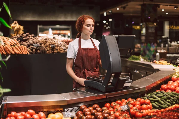 Önlük ayakta modern süpermarkette çalışma sebze ile tezgahın arkasındaki genç satıcı