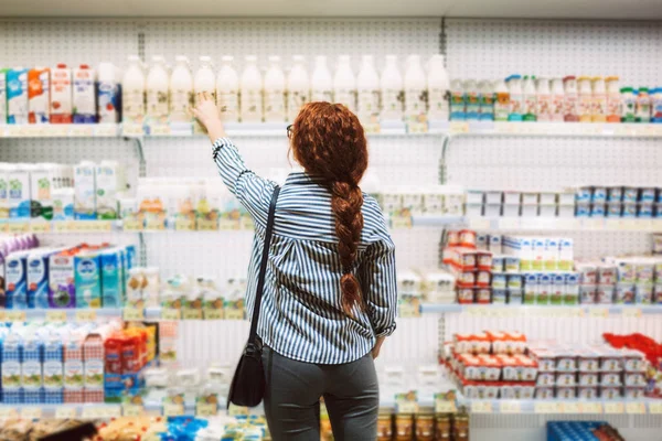穿条纹衬衫的年轻妇女从后面选择现代超市的乳制品 — 图库照片