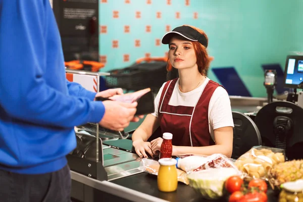 Unga Kvinnliga Kassören Uniform Eftertänksamt Tittar Kunden Arbetar Modern Stormarknad — Stockfoto