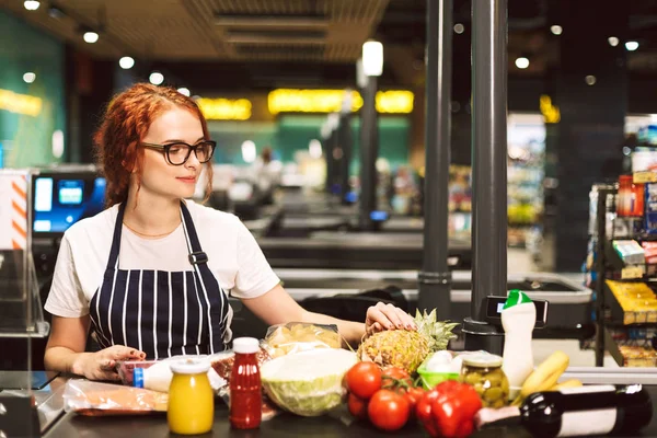 Unga Kvinnliga Kassören Glasögon Och Randigt Förkläde Med Produkter Kontanter — Stockfoto