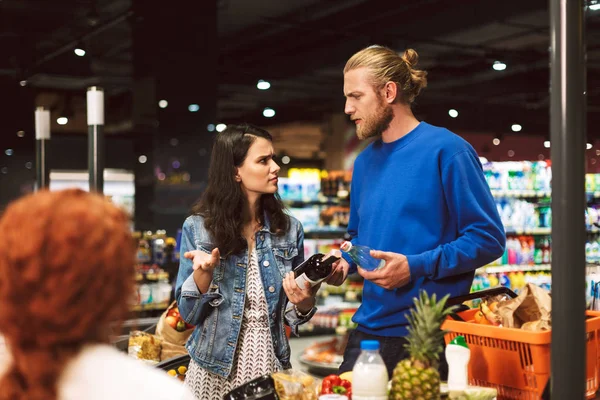 Young couple near cashier desk emotionally discussing something in modern supermarket