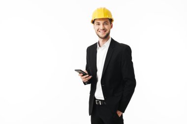 Arka plan beyaz bussinesman mutlu bir şekilde fotoğraf makinesi holding cellphone elinde üzeri sarı Emanet kask içinde gülümseyen genç