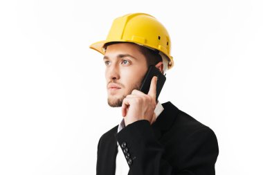 Düşünceli bir kenara beyaz arka plan üzerinde telefonda konuşurken sarı Emanet kask içinde genç ciddi bussinesman
