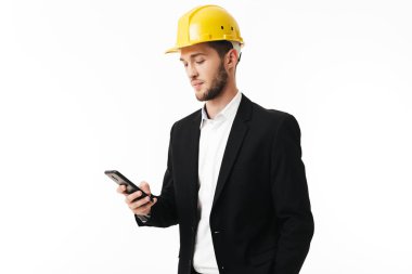 Cep telefonu elinde beyaz arka plan üzerinde tutan Sarı kask içinde genç düşünceli bussinesman