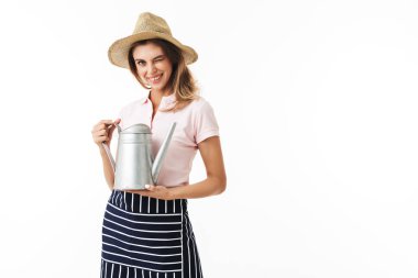 Genç gülümseyen kadın hasır şapka ve çizgili önlük mutlu beyaz arka plan üzerinde elele sulama pot fotoğraf makinesinde göz kırpıyor