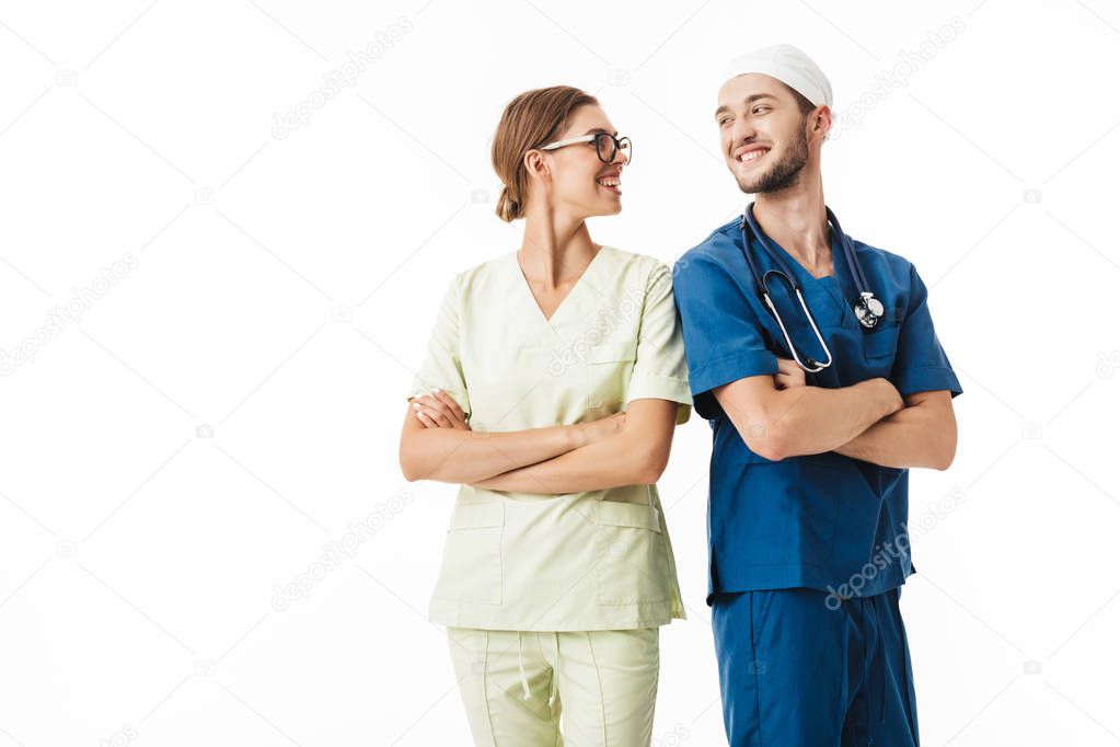 Young smiling doctor with phonendoscope on neck and pretty nurse in eyeglasses and uniform happily looking at each other over white background