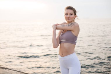 Sportif üst ve beyaz tozluk pratik yoga arka plan üzerinde güzel deniz manzaralı güzel kız. Düşünceli bir yana deniz kıyısında uzanan arayan genç kadın