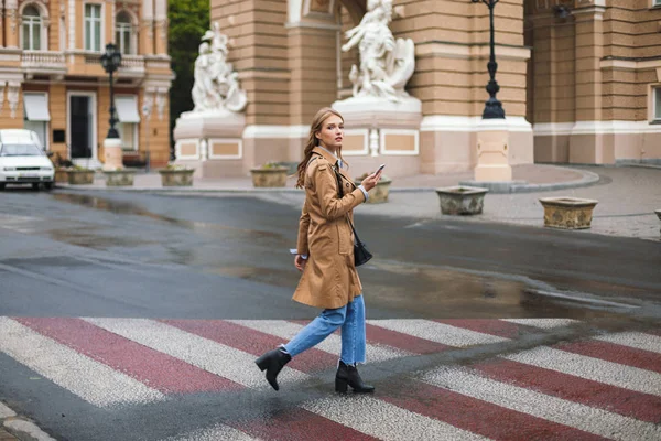 Młoda Piękna Kobieta Płaszczu Dżinsy Starannie Patrząc Aparacie Gospodarstwa Telefon — Zdjęcie stockowe