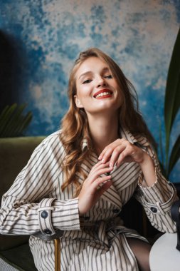 Çizgili trençkot mutlu seyir fotoğraf makinesindeki harcama zaman modern kafede dalgalı saçlı genç çekici gülümseyen kadın