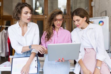 Grup Genç şık kadını amazedly laptop modern rahat Office birlikte çalışma. Düşünceli kızlar iş başında vakit