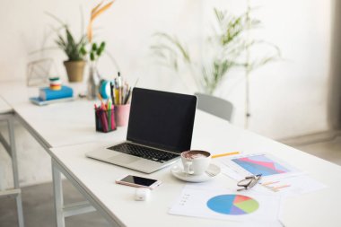 Laptop ve beyaz fincan kahve modern boş ofiste masa üzerinde fotoğraf. Konforlu ve rahat çalışma alanı