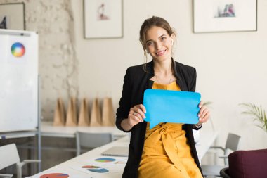 Siyah ceket ve radyo earphones sersem kamera tutan mavi kağıt şeklinde mesaj elinde modern ofis çalışmalarında bakarak masasında oturan genç güzel gülümseyen kadın
