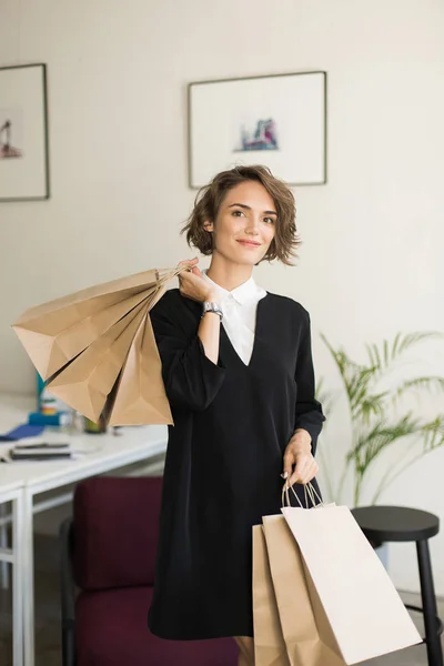 Menina Sorridente Bonita Vestido Preto Sonhadoramente Olhando Câmera Segurando Pacotes — Fotografia de Stock