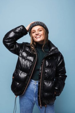 Genç güzel gülümseyen kadın örgü şapka ve siyah ceket mutlu kamera seyir üzerinde mavi arka plan aşağı