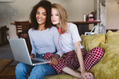 Genç gülümseyen Afrikalı-Amerikalı kadın siyah kıvırcık saçlı ve diz ve sarı saçları ve kırmızı kulaklık sersem kamera birlikte evde arıyorum güzel kadınla üstünde laptop