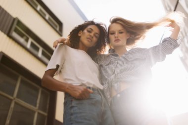 Karanlık kıvırcık saç T-shirt ve güzel kadın düşünceli seyir fotoğraf makinesindeki harcama zaman birlikte gömlekli sarışın saçlı genç çekici Afrikalı-Amerikalı kadın açık