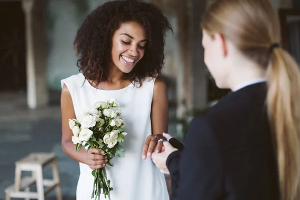 美丽的非洲裔美国妇女与深色卷曲的头发在白色的礼服举行小花束花在手愉快地花时间在婚礼仪式上 — 图库照片