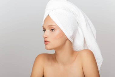 Düşünceli bir kenara kapatıcı krem yanağına gri arka plan üzerinde seyir makyaj olmadan başında beyaz havlu ile genç güzel kadın portresi