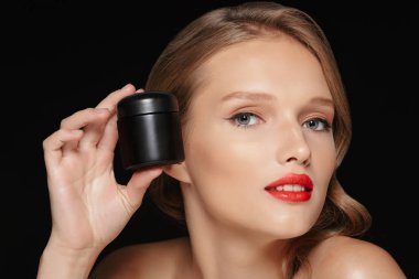 Dalgalı saç ve güzellik kremi el yakınındaki sersem kamera seyir siyah arka plan üzerinde yüz tutan kırmızı dudaklar ile genç güzel kadın portresi