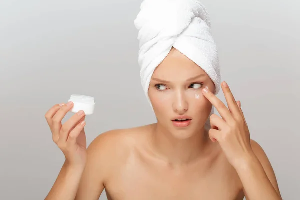 白タオル頭顔の思慮深くよそ見灰色の背景の上にクリームを適用することの上で化粧をせず深刻な女性の肖像画 — ストック写真