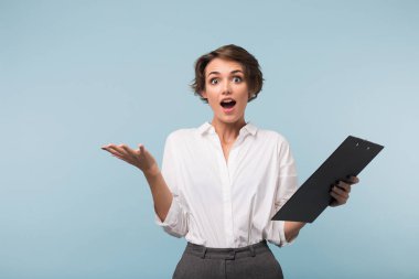 El amazedly kamera seyir üzerinde mavi arka plan beyaz gömlek holding klasöründe siyah kısa saçlı bayanla genç şaşırttı