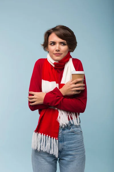 脇は青い背景に寒さから揺れを思慮深く探して手に赤いセーターとスカーフ持株一杯のコーヒーで若い女性 — ストック写真