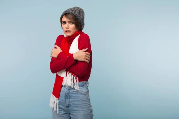 赤のセーター スカーフ ニット帽子が悲しいことに青い背景によそ見寒さから揺れの短い黒髪の若い不健康な女性 — ストック写真