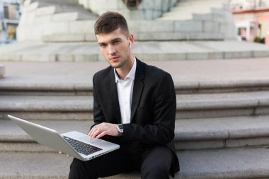 Düşünceli kamera seyir holding dizüstü eller açık radyo earphones ile klasik siyah elbiseli Genç yakışıklı işadamı