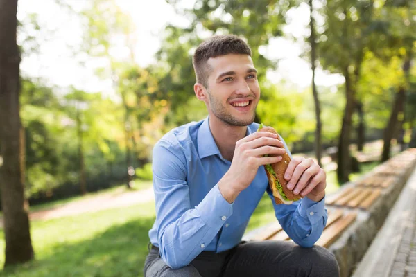 Young Cheerful Man Blue Shirt Sitting Bench Sandwich Hands Happily — Stock Photo, Image
