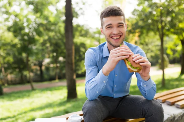 Giovane Uomo Ridente Camicia Blu Seduto Sulla Panchina Con Panino — Foto Stock