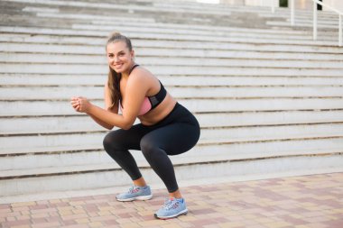 Young pretty smiling plus size woman in sporty top and leggings doing sport with stairs on background outdoor clipart