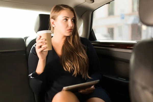 Young Pensive Businesswoman Black Dress Sitting Back Seat Car Tablet — Stockfoto