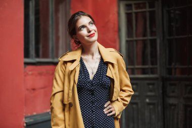 Genç güzel gülümseyen kadın elbise ve trençkot sersem bir yana ayakta açık arka plan eski kapı ile seyir