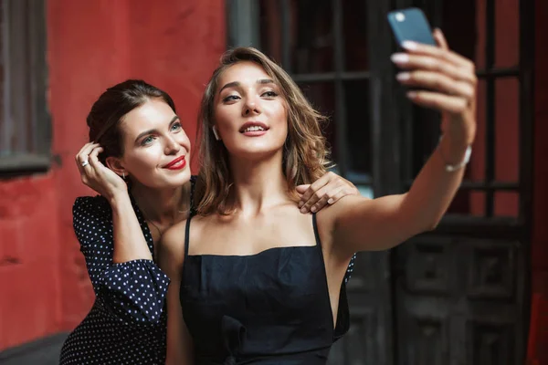 Дві Молоді Красиві Жінки Чорних Сукнях Мрійливо Фотографують Мобільний Телефон — стокове фото