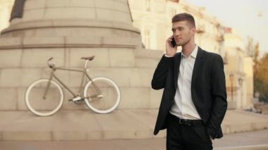 Cep telefonu cep daimi bir Şehir Meydanı anıt arka planda bir bisiklet ile elini tutarak iyi haber alma siyah elbiseli genç yakışıklı işadamı