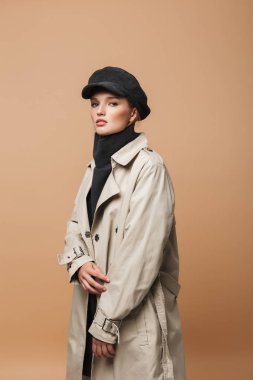 Genç güzel dalgın kadın klasik trençkot ve sensually kamera seyir bej renkli arka plan üzerinde kap