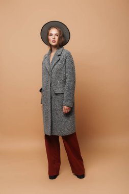 Sersem kamera bej renkli arka plan üzerinde seyir şapka gri ceket ve geniş olan muhteşem kadın pantolon