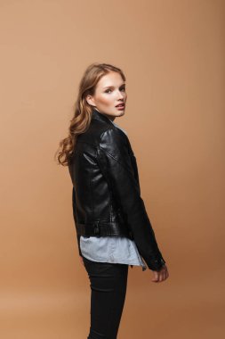 Dalgalı saç siyah deri ceket ve gömlek sersem kamera bej renkli arka plan üzerinde seyir ile genç güzel Bayan