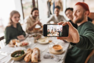 Grup çekici uluslararası arkadaşıyla birlikte vakit yemekle masadan. Genç meslektaşları sevinçle rahat kafede yemeğe modern cep telefonu üzerinde fotoğraf çekme