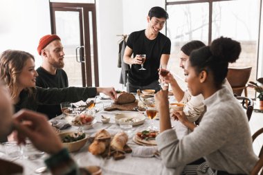 Neşeli Asya genç gözlük ve siyah tişört holding kadeh şarap elinde. Mutlu birlikte rahat beyaz kafede öğle üzerinde vakit çekici uluslararası arkadaş grubu