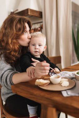 Örme kazak kamera sersem arıyor o küçük oğlunu kafasından öpüşme yemekle masadan Kızıl saçlı genç güzel kadın. Anne ile bebek evde rahat mutfakta vakit