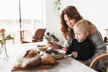 Örme kazak sersem küçük oğlu evde rahat mutfakta vakit besleme masada oturan Kızıl saçlı genç güzel anne