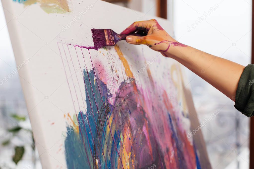 Close up photo of woman hands in paints holding paintbrush drawi