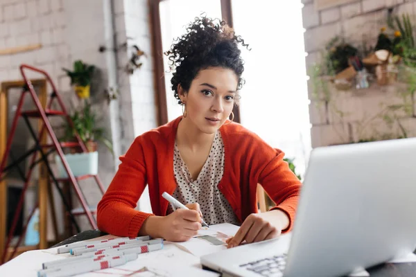 Junge attraktive Frau mit dunklem lockigem Haar sitzt am Tisch — Stockfoto