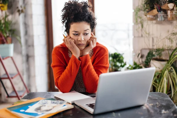 Junge ernste Frau mit dunklem lockigem Haar am Tisch sitzend le — Stockfoto