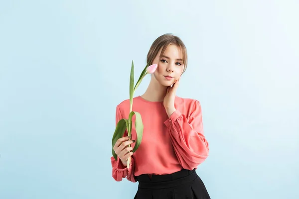 Ung, vakker jente i bluse som holder rosa tulipan i hånden nær f – stockfoto
